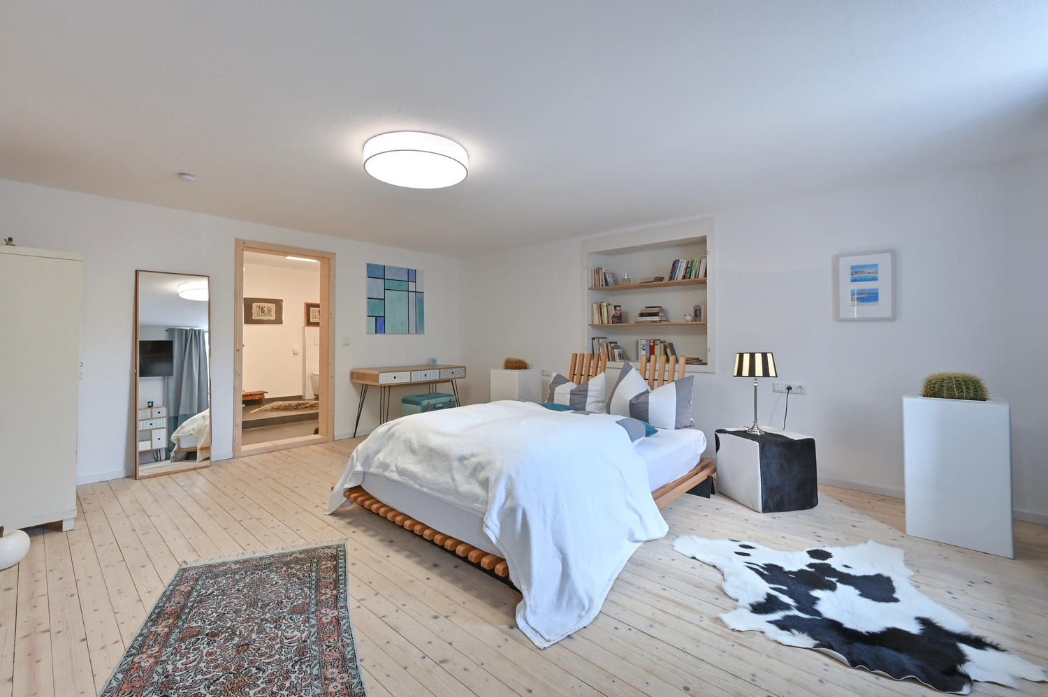Antjes – Roomstyling –  Nachher: Ein helles Schlafzimmer mit weiß gestrichenen Wänden, Holzboden, einem großen Bett, Teppichen und modernen Deko-Elementen.