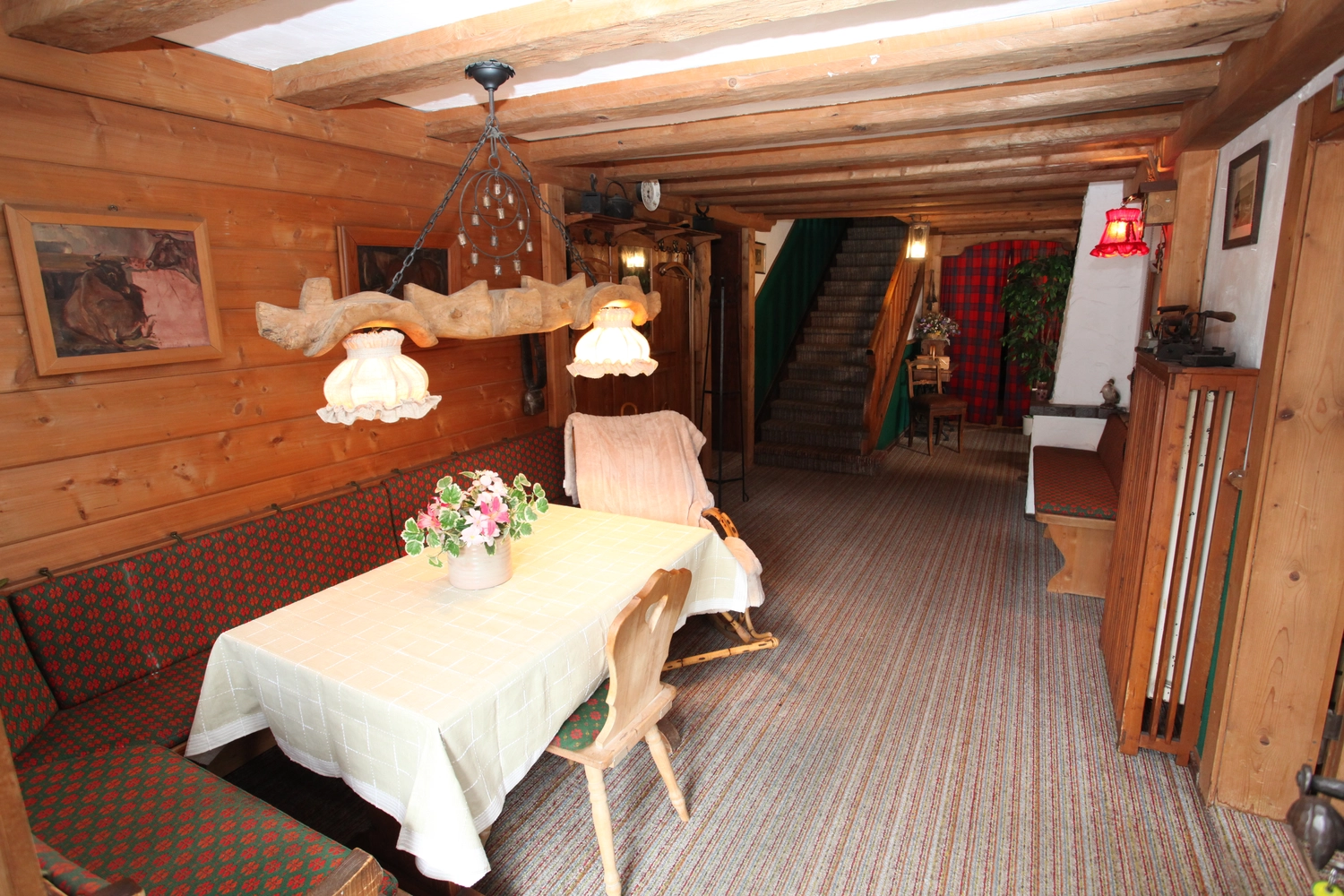Antjes – Roomstyling –  Vorher: Ein rustikaler Essbereich mit Holzwänden, Eckbank, weißer Tischdecke und gemütlicher Treppe im Hintergrund.