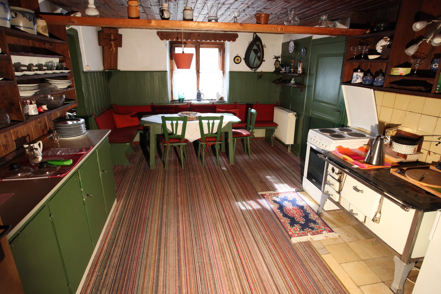 Antjes – Roomstyling –  Vorher: Eine rustikale Küche mit grünen Schränken, roter Eckbank, Holzbalkendecke und Fliesenboden.
