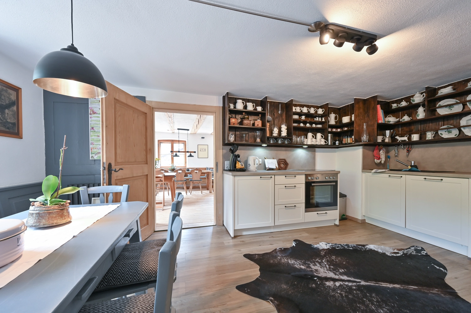 Antjes – Roomstyling –  Nachher:Eine moderne helle Küche mit weißen und Holzschränken, Esstisch, Holzboden, Kuhfell-Teppich und offener Wohnbereich-Anbindung.