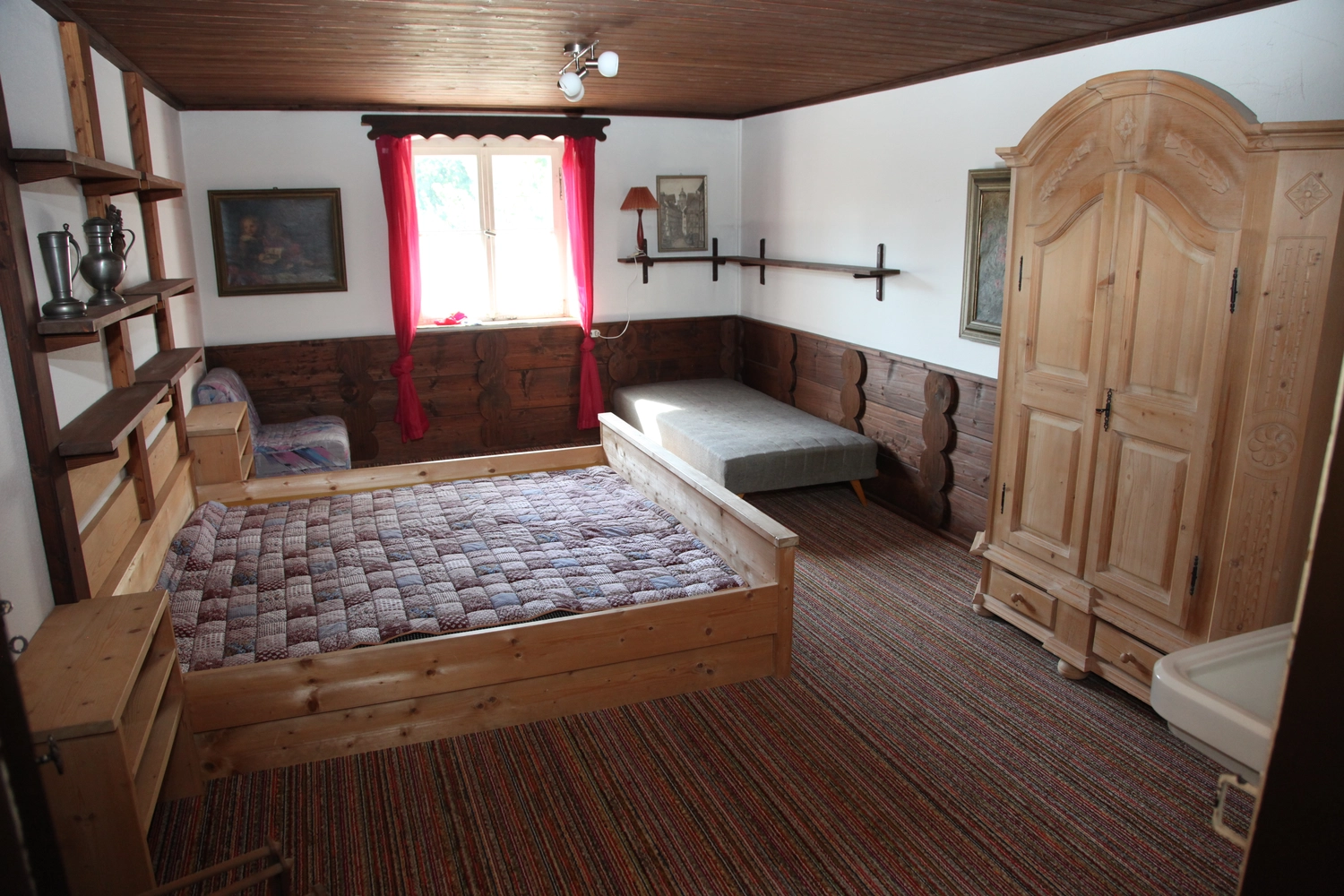 Antjes – Roomstyling –  Vorher:Ein rustikales Schlafzimmer mit zwei Einzelbetten, Holzvertäfelung, braunem Teppich und roten Vorhängen.