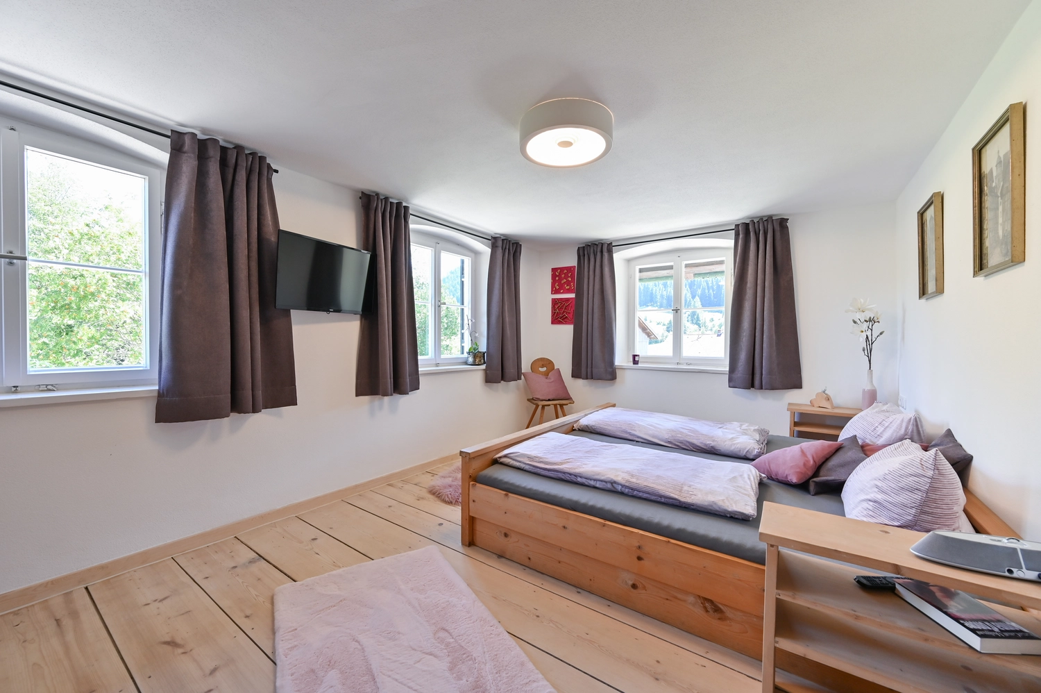 Nachher – Ein helles, modernes Schlafzimmer mit weißen Wänden, grauen Vorhängen, einem Doppelbett aus Holz und minimalistischer Einrichtung mit Teppich und Fernseher.