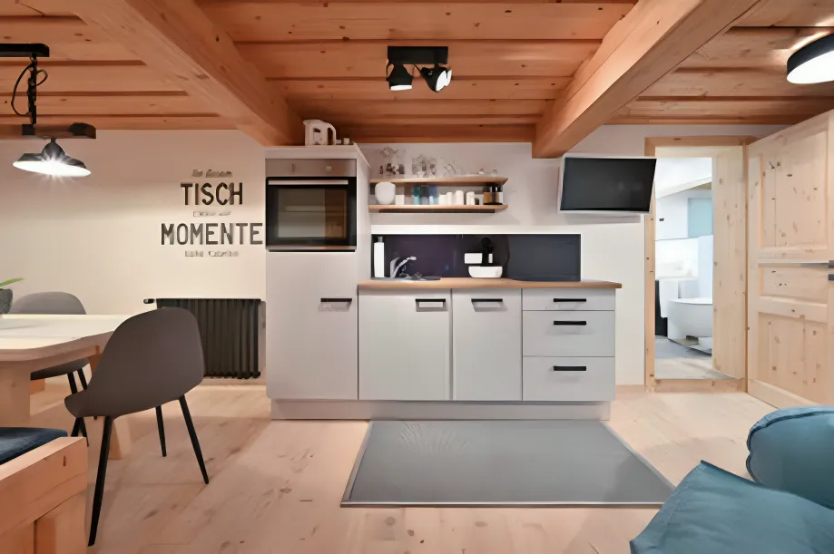 Antjes – Roomstyling – Eine helle, rustikale Küche mit Holzbalken, weißen Schränken, einem Esstisch und gemütlicher Dekoration im alpinen Stil.